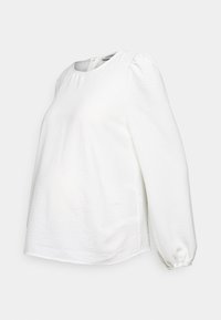 Blouse blanche à manches longues avec épaules bouffantes, encolure ronde et poignets froncés, présentée sur un fond clair uni.