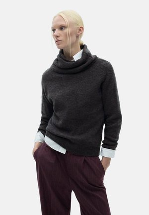 Donkergrijze coltrui van zacht materiaal, met een losse pasvorm en een opgerolde halslijn, gecombineerd met bordeauxrode broek met streepjes en een wit shirt.