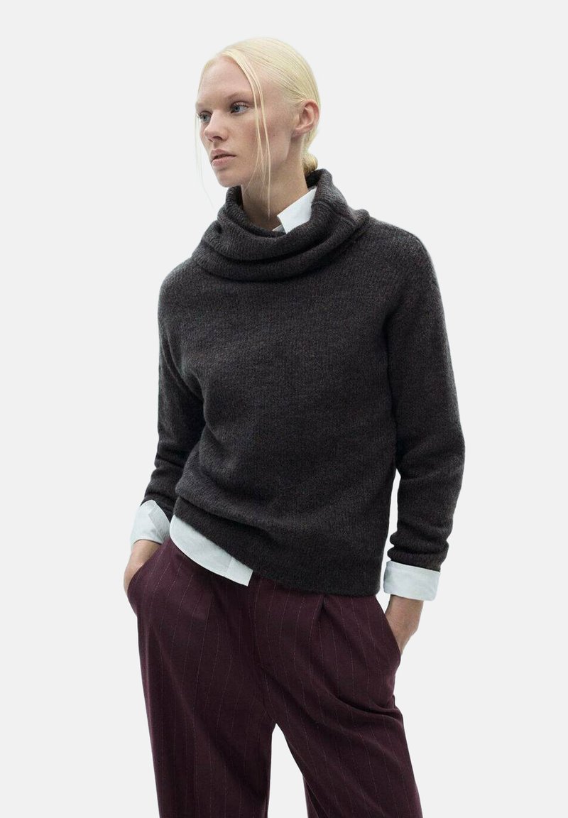 Ciemnoszary sweter typu golf w miękkim materiale, o luźnym kroju i zwiniętym dekolcie, zestawiony z bordowymi spodniami w prążki oraz białą koszulą.