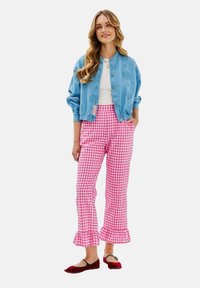 Světle modrá džínová bunda s knoflíky, bílý top, růžové kárované kalhoty s volánovým lemem a červené baleríny s kontrastním páskem.