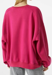 Sudadera extragrande en un vibrante color rosa. Confeccionada en un tejido suave con puños y bajo acanalados. Presenta un cuello redondo y hombros caídos.