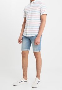 Camisa de manga corta a rayas en colores pastel, pantalones cortos de denim azul con dobladillos enrollados y zapatillas blancas con acentos azules.