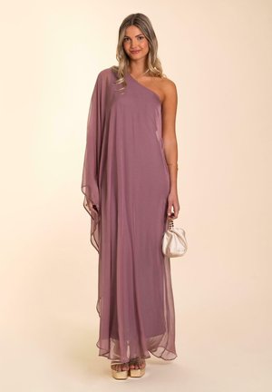 Robe maxi longue à une épaule en tissu rose pâle, avec un design fluide. Associée à une petite pochette crème et des sandales à plateforme dorées.