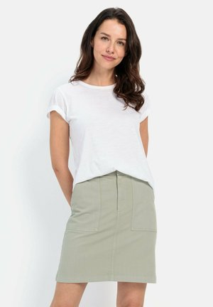 Witte T-shirt met korte mouwen, gecombineerd met een olijfgroene rok tot de knie met twee voorzakken en een soepele textuur. Eenvoudig ontwerp.