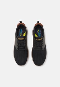 Schwarze Sportschuhe mit Mesh-Obermaterial, Gummisohle und Schnürsenkeln. Verfügt über einen braunen Fersenpatch und eine kontrastierende gelbe Einlegesohle.