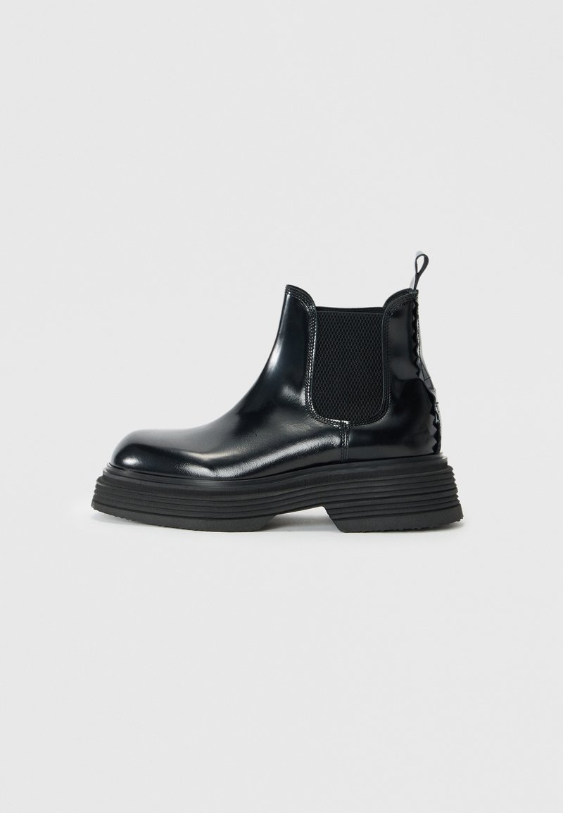 Bottines Chelsea en cuir noir avec une finition lisse, des panneaux latéraux en élastique et une semelle en caoutchouc épaisse et texturée. Équipées d'une languette pour un enfilage facile.
