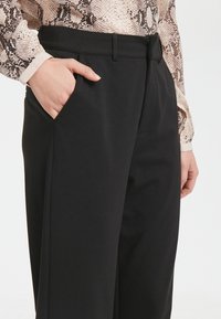 Černé konstruktérské kalhoty s hladkou texturou, opatřené páskem, bočními kapsami a rovnými nohavicemi.