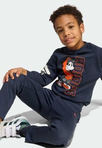Marineblauwe trainingspak met een cartoonfiguur op het shirt, voorzien van witte en oranje accenten; gestructureerde stof, relaxte pasvorm en lichtgewicht ontwerp.