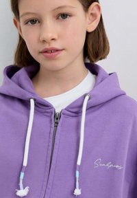 Fioletowa bluza z kapturem na zamek błyskawiczny z białymi sznurkami, z haftowanym napisem na piersi i miękkim, teksturowanym materiałem.