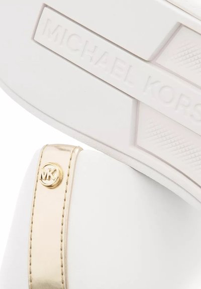 Baskets blanches avec une surface lisse, sangle d'accent dorée arborant un logo circulaire, semelle texturée et nom de la marque embossé sur le côté.
