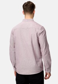 Chemise à manches longues en tissu texturé rose clair avec un col à boutons, un ourlet incurvé et des poignets à boutons, vue de dos.