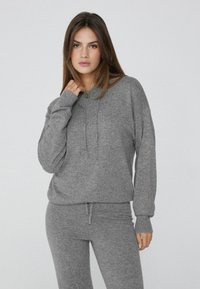 Grauer Hoodie und passende Hose aus weichem Stoff. Der Hoodie hat eine Kordel und gerippte Bündchen; beide haben einen lässigen Schnitt und eine glatte Textur.