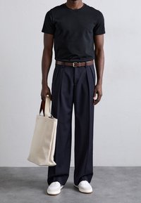 Czarna bawełniana koszulka, granatowe spodnie w kant, brązowy skórzany pasek, białe sneakersy oraz beżowa torba na ramię z brązowymi uchwytami.