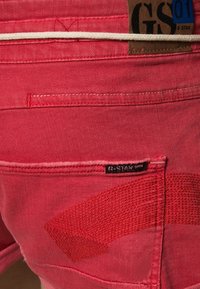 Pantalones cortos de mezclilla roja con detalles de parches, etiqueta de G-Star y costuras en contraste. Presentan una textura suave y sutiles acentos tejidos.