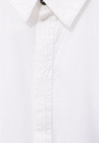 Camisa blanca de cuello con un cierre de botones oculto y un sutil bordado de rayo a lo largo de la costura frontal.