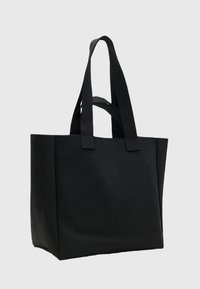 Sac fourre-tout noir en toile avec deux poignées robustes, de forme rectangulaire et une poche avant plate. Dispose d'un tissu texturé et de lignes épurées.