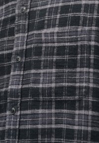 Καρό φανελένιο πουκάμισο σε μαύρο και γκρι, με απαλή υφή, κούμπωμα με κουμπιά και τσέπη στο στήθος με οριζόντιες ρίγες.