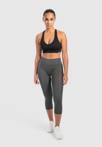 Top corto sportivo nero con scollatura ampia e design racerback, abbinato a leggings capri grigi a vita alta e sneakers bianche.