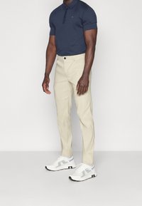 Námořnické polo tričko s krátkým rukávem a stylovým límcem, spárované s béžovými slim-fit kalhotami a bílými teniskami s šedými akcenty.