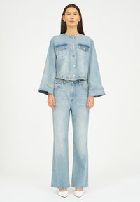 Ljusblå denimjacka med två bröstfickor, silverfärgade knappar och utsvängda ärmar, i kombination med matchande högmidjade jeans med utsvängda ben.