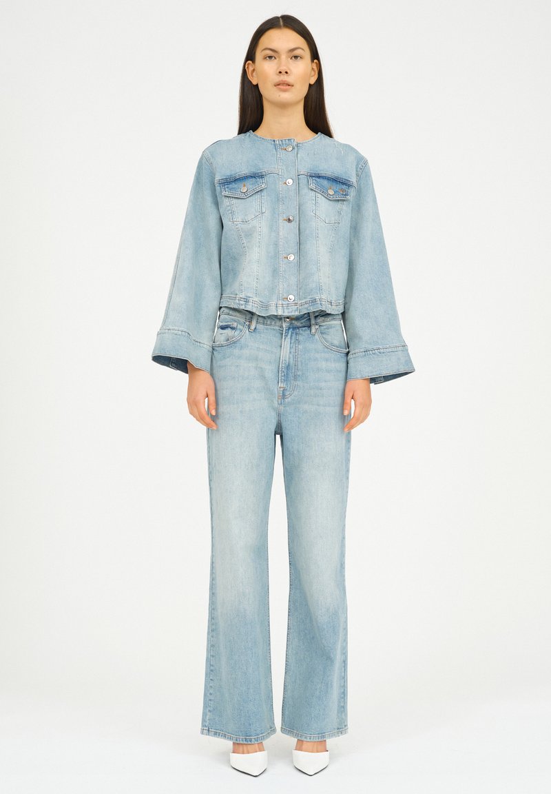 Ljusblå denimjacka med två bröstfickor, silverfärgade knappar och utsvängda ärmar, i kombination med matchande högmidjade jeans med utsvängda ben.