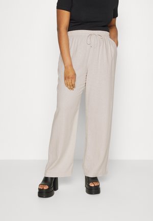 Person trägt beige weite Hosen mit elastischem Bund und Kordelzug, kombiniert mit schwarzen Plateau-Sandalen mit offener Zehenpartie und schwarzem Kurzarmtop.