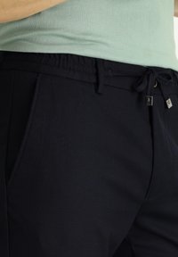 Marineblauwe broek met een elastische tailleband, trekkoordsluiting en zijzakken. Glad oppervlak, met kleine metalen accenten.