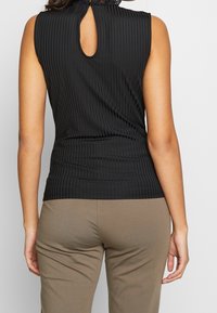 Haut noir sans manches avec texture côtelée verticale et détail de découpe en forme de clé au dos. Associé à un pantalon ajusté brun clair.