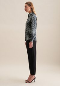 Camicetta con bottoni, motivo a catena blu navy e bianco, maniche lunghe, abbinata a pantaloni neri a sigaretta e sandali neri con tacco.