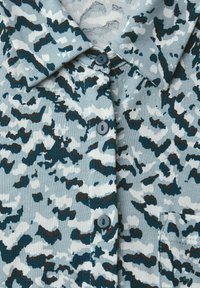 Camicia a maniche corte di colore azzurro chiaro, con un motivo camouflage casual in blu scuro e bianco. Include un colletto e tre bottoni.