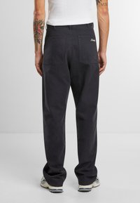 Pantalones rectos de color gris oscuro con una textura suave, dos bolsillos traseros y un logotipo bordado sobre el bolsillo derecho.