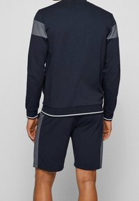 Marinblå sweatshirt- och shorts-set i mjukt tyg. Sweatshirten har gråa axelaccenter och vit kant. Shortsen är i en solid marinblå färg.