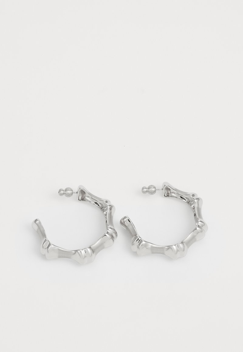 Srebrne kolczyki w kształcie obręczy z teksturowanym, nierównym wzorem. Wykonane z metalu, z bezpiecznym zapięciem na sztyft oraz polerowanym wykończeniem.