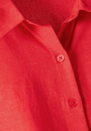 Czerwona lniana koszula z guzikiem z kołnierzykiem, z pojedynczym guzikiem o czterech otworach i teksturowaną powierzchnią materiału.