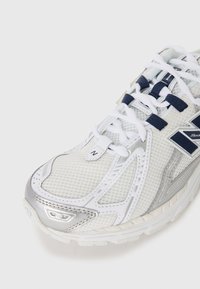 White mesh running shoe with silver accents. Features padded tongue, navy laces, and textured rubber sole. Lightweight design for comfort.