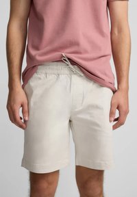 Pantalones cortos beige de tela ligera, con una cintura elástica con cordón, bolsillos laterales y un corte simple.