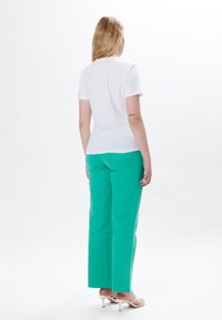 Camiseta blanca de manga corta, combinada con pantalones turquesas de cintura alta y pierna ancha. Textura suave; diseño minimalista; sin patrones visibles.