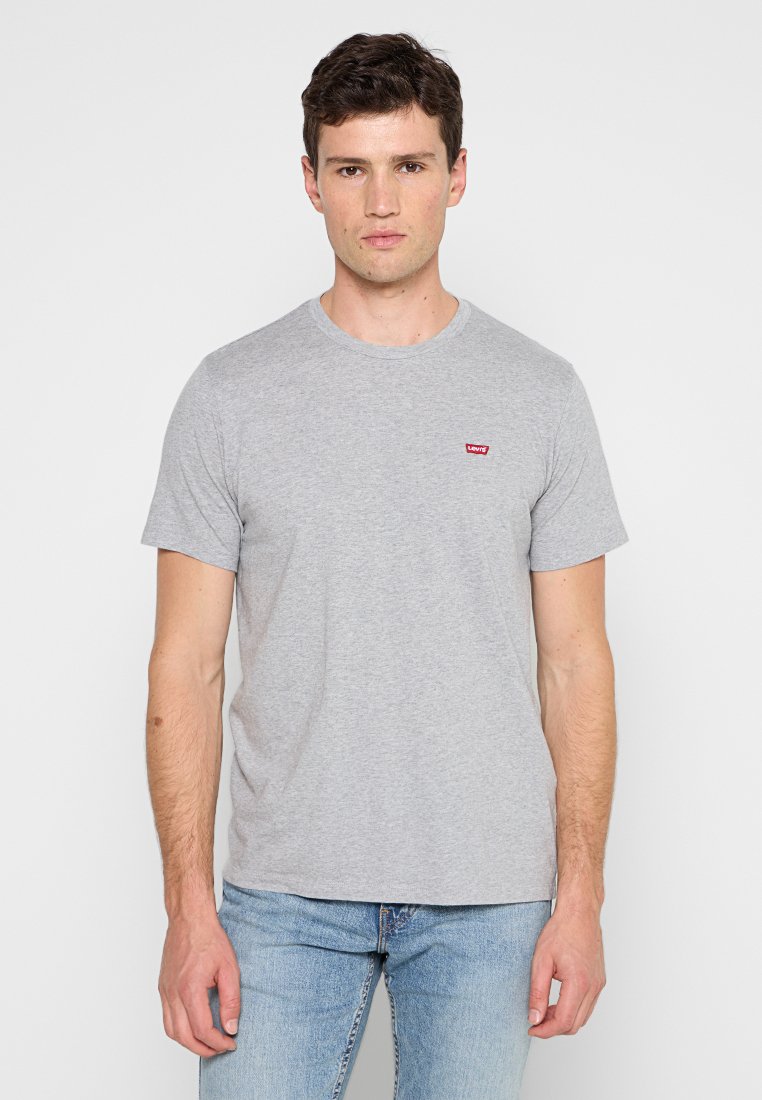 Szara bawełniana koszulka z krótkimi rękawami, okrągłym dekoltem i małym czerwonym logo Levi's na lewej piersi, zestawiona z jasnoniebieskimi dżinsami.