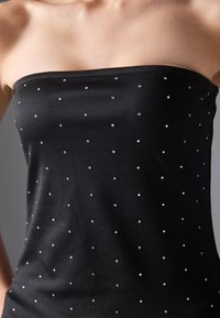 Top negro sin tirantes hecho de una tela suave, adornado con pequeños strass espaciados uniformemente para un efecto brillante.