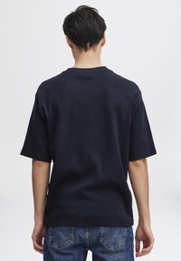 Tricou de culoare bleumarin, cu mâneci scurte și guler rotund. Textură ribbită și croială lejeră, asortat cu blugi din denim de culoare albastru deschis.