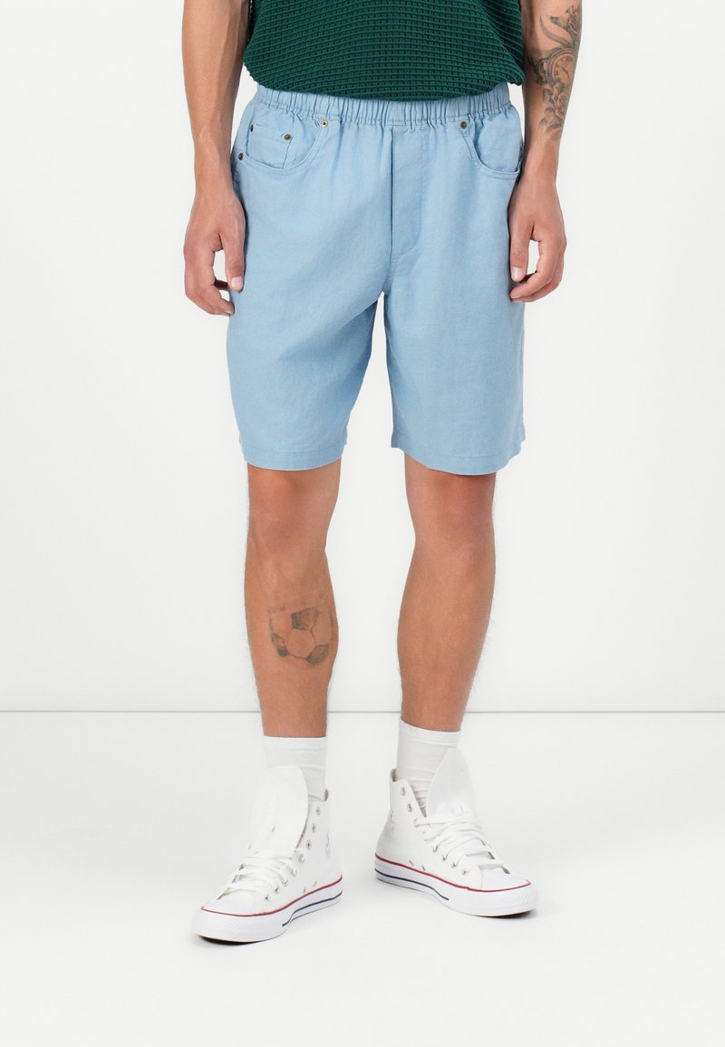 Shorts bleu clair avec taille élastique, poches latérales et coupe décontractée, associés à des baskets montantes blanches et des chaussettes de longueur crew.