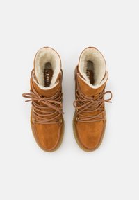 Botas de ante marrón con forro de piel sintética, punta redondeada y detalles en dorado. Cuentan con cordones marrones y una suela exterior de goma texturizada.