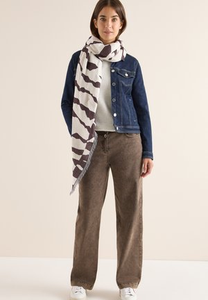 Veste en denim, écharpe blanche à motifs avec des rayures marron foncé, pull en tricot texturé, pantalon large marron, et baskets blanches.