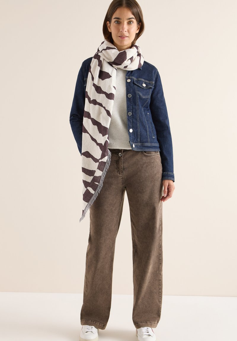 Giacca di jeans, sciarpa bianca a motivi con strisce marroni scure, maglione lavorato a punto, pantaloni marroni a gamba larga e sneakers bianche.
