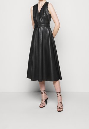 Czarna silikonowa sukienka midi bez rękawów z dekoltem w kształcie litery V, paskiem w talii i spódnicą w kształcie litery A, zestawiona z czarnymi sandałami na obcasie z wiązaniami.