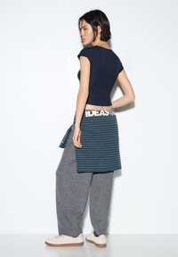 Námořnický přiléhavý top, šedé široké kalhoty a proužkovaná sukně uvázaná v pase. Bílé tenisky s béžovými akcenty. Hladká tkanina a uvolněný design.