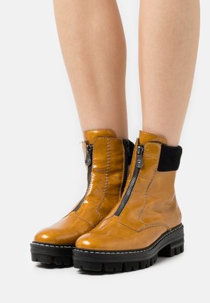 Yellow patent leather ankle boots with black fabric accents and zippers; chunky black rubber sole with textured tread pattern.