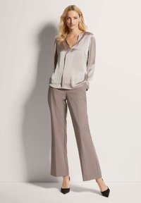 Zijden blouse in lichtgrijs met een V-hals en lange mouwen, gecombineerd met beige wijde broekspijpen en zwarte puntige hakken.