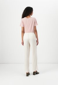 Light pink short-sleeve top with a V-neck, paired with loose-fitting, cream-colored trousers and green heeled shoes. Neutral background.