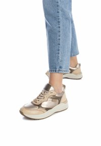 Zapatillas beige y doradas metálicas con parte superior texturizada, suela acolchada y diseño de cordones. Los acentos incluyen el logotipo y materiales en contraste.